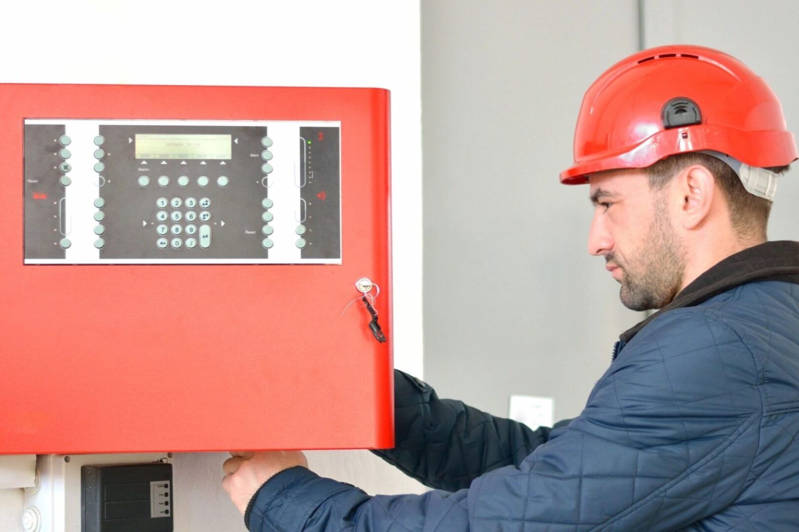 A man in red hard hat holding up a fire alarm.